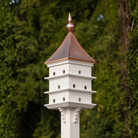 Classic Purple Martin white birdhouse with a copper roof against a green tree background