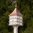 Grand estate Purple Martin birdhouse with a copper roof against a green foliage background
