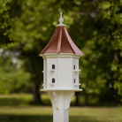 Decorative birdhouse with multiple double entry points and a sloped copper roof against a green blurred background