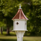 White birdhouse with a copper roof in a garden setting