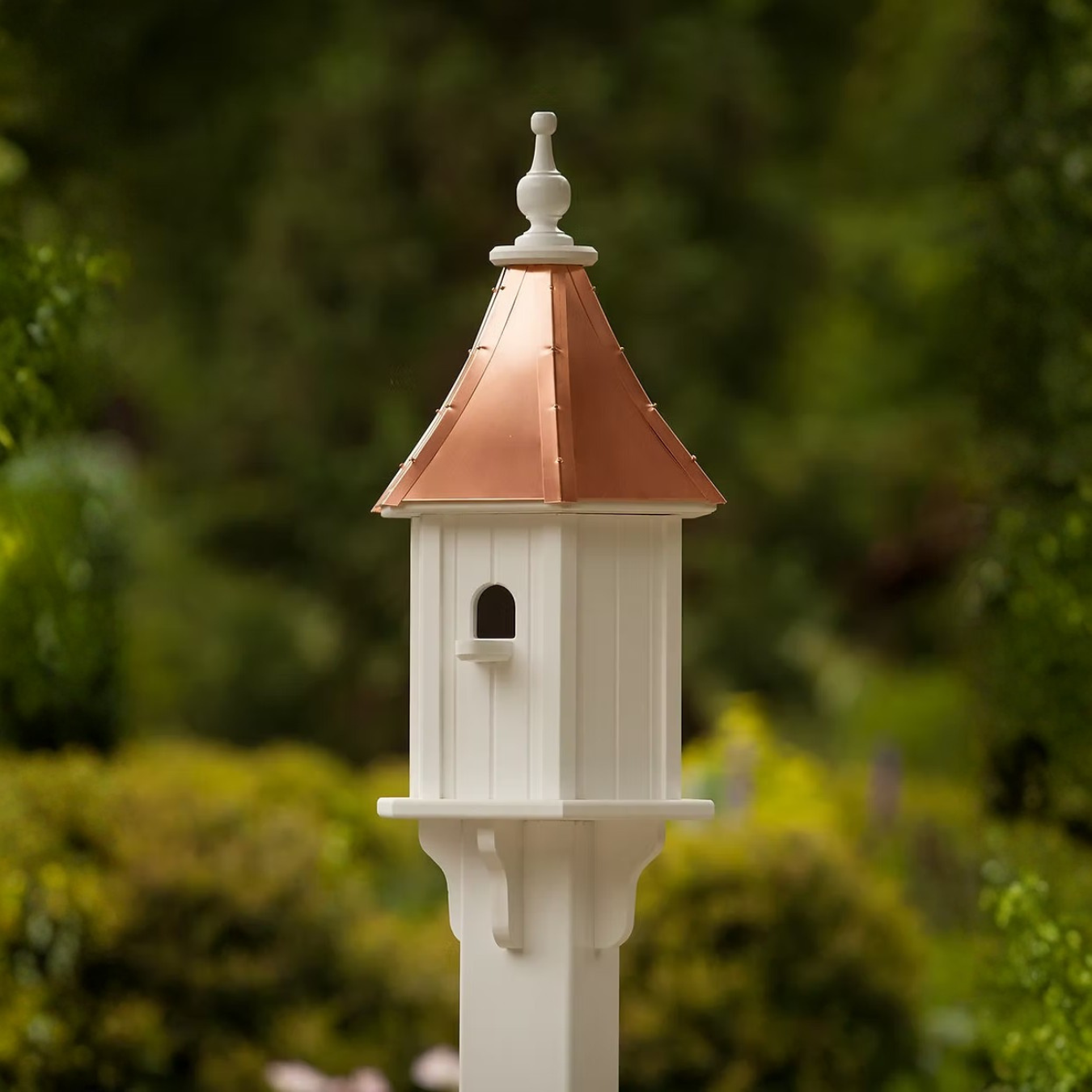 White birdhouse with a copper roof against a green blurred background