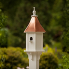 White birdhouse with a copper roof against a green blurred background