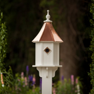 Decorative birdhouse with a copper roof in a garden setting