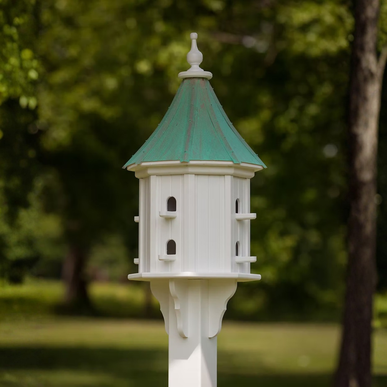 White birdhouse with multiple perch openings with a patina copper roof in a garden setting