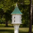 White birdhouse with multiple perch openings with a patina copper roof in a garden setting