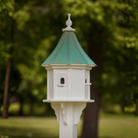 White birdhouse with multi entry perches and a patina copper roof in a garden setting