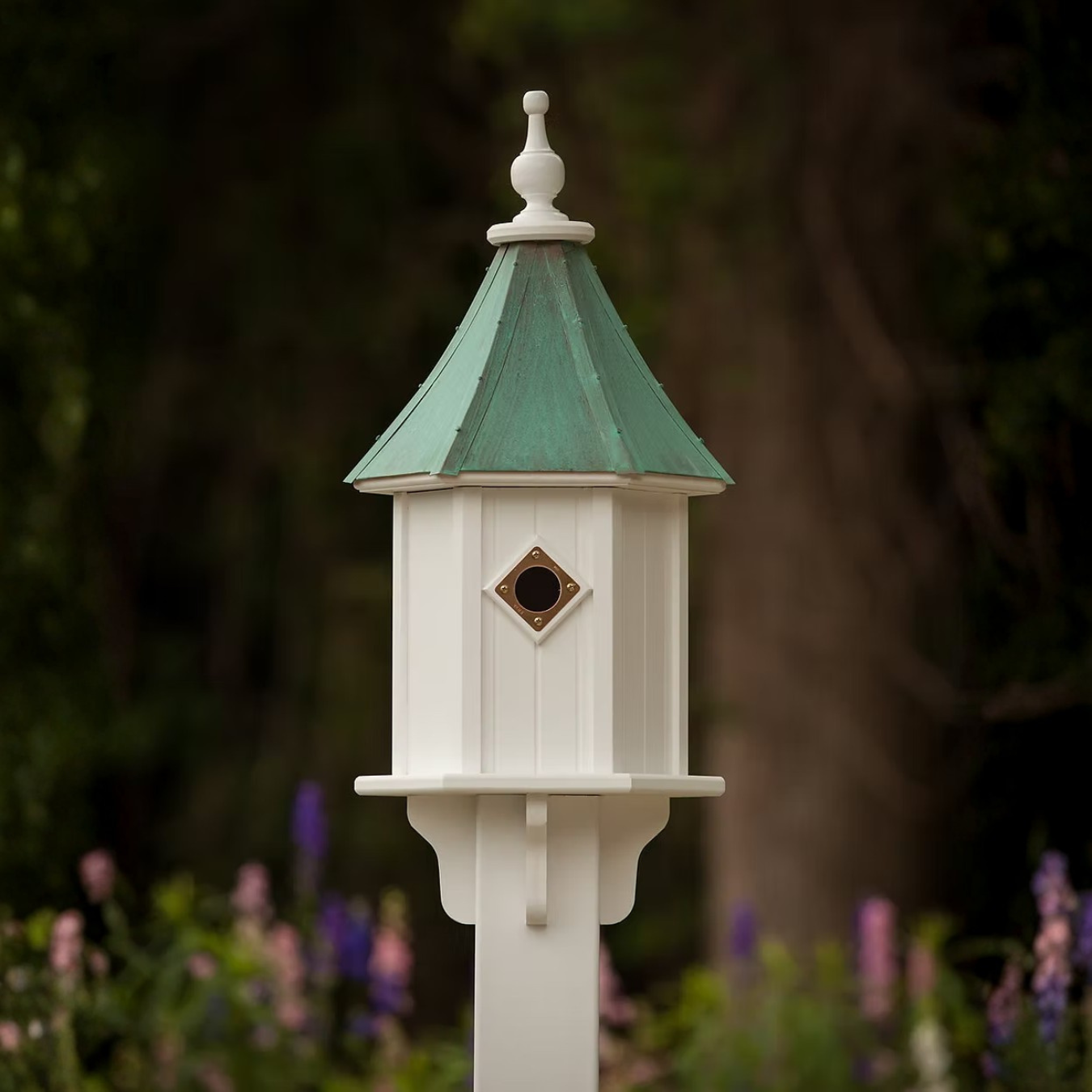 White birdhouse with a copper portal and a patina copper roof in a garden setting
