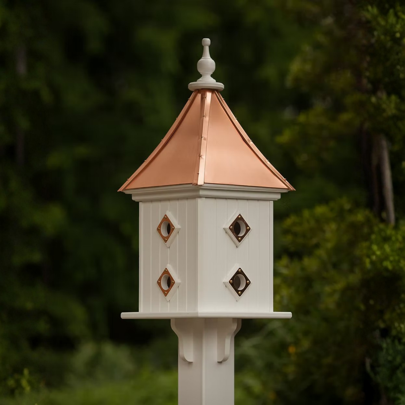 Decorative square birdhouse with double copper portal entries and a copper roof against a blurred green background