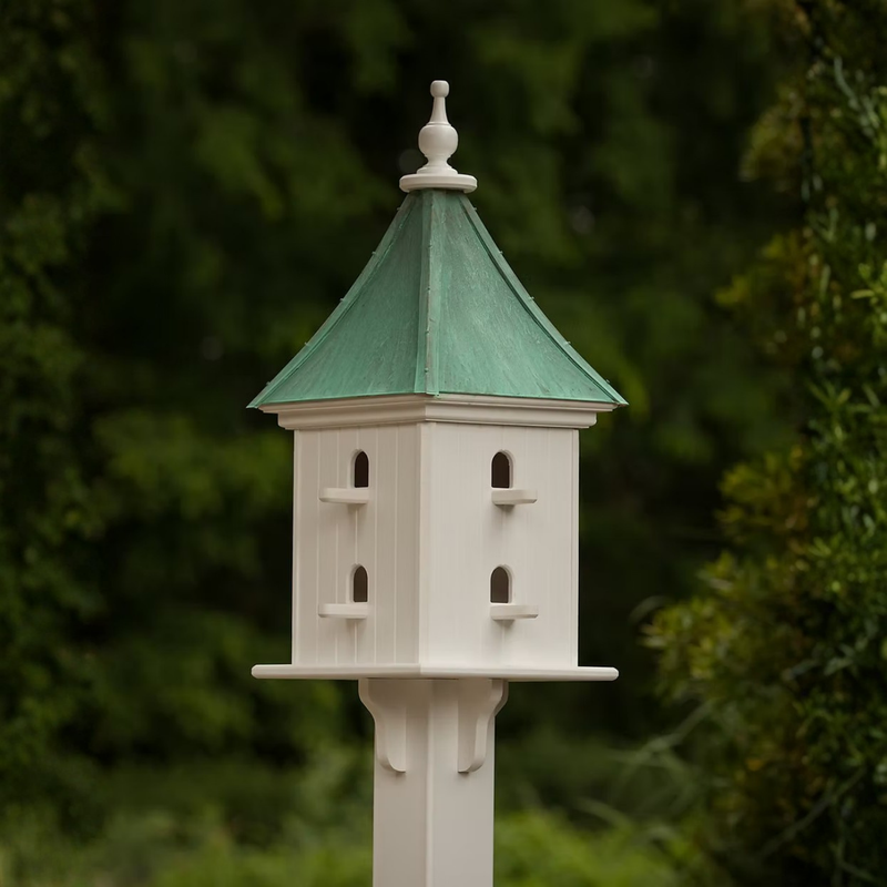 White square birdhouse with double entry perches and a patina copper sloped roof against a blurred green background