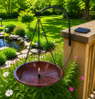 Bird bath hanging on a metal stand in a garden setting with flowers and a wooden deck.