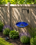 Blue bird bath hanging on a wooden fence with plants and grass below