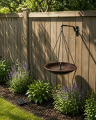 Rustic metal bird bath hanging on a wooden fence with plants and grass below