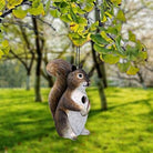 Squirrel-shaped bird feeder hanging from a tree branch with a blurred green garden background