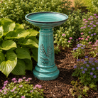teal ceramic bird bath sitting in a bed of flowers and hostas