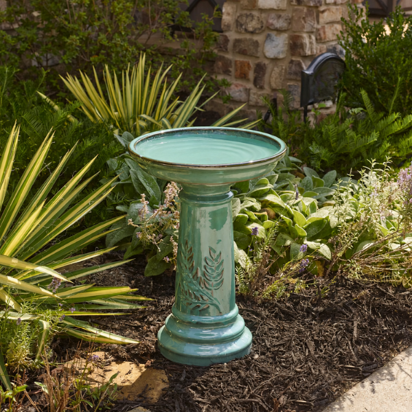 teal ceramic birdbath sitting in a garden with greenery 