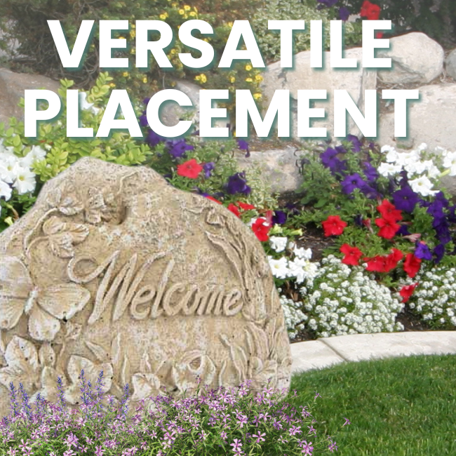 "Welcome" stone placed in a vibrant garden bed with flowers and greenery.