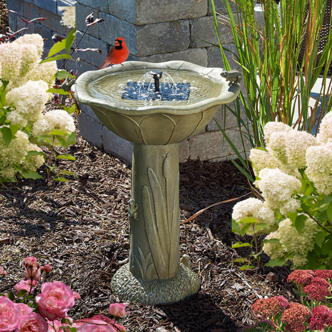 A beautifully detailed birdbath with a solar-powered fountain, surrounded by flowers, attracting a red cardinal.