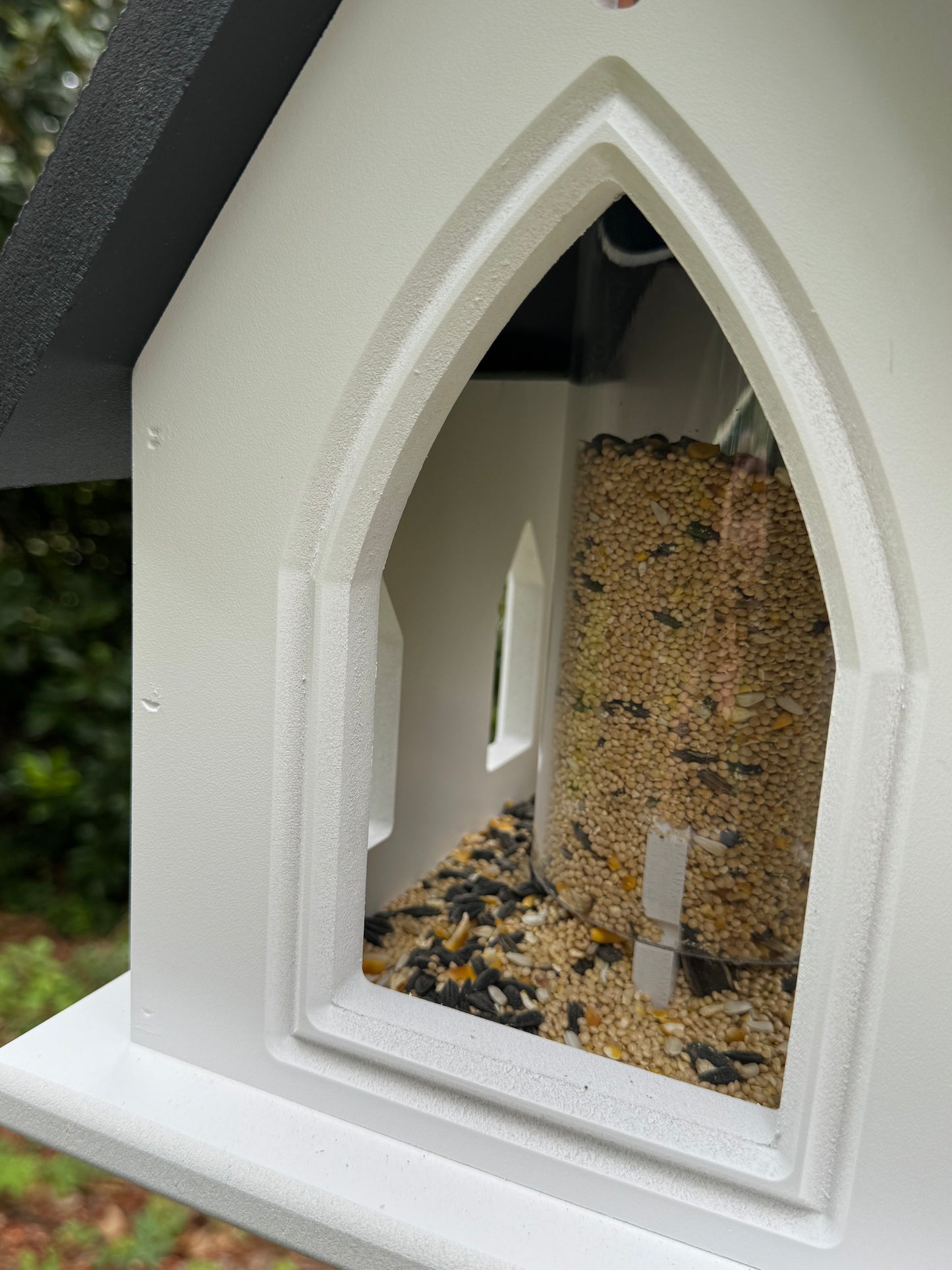 White bird feeder with seed inside, set against a blurred natural background
