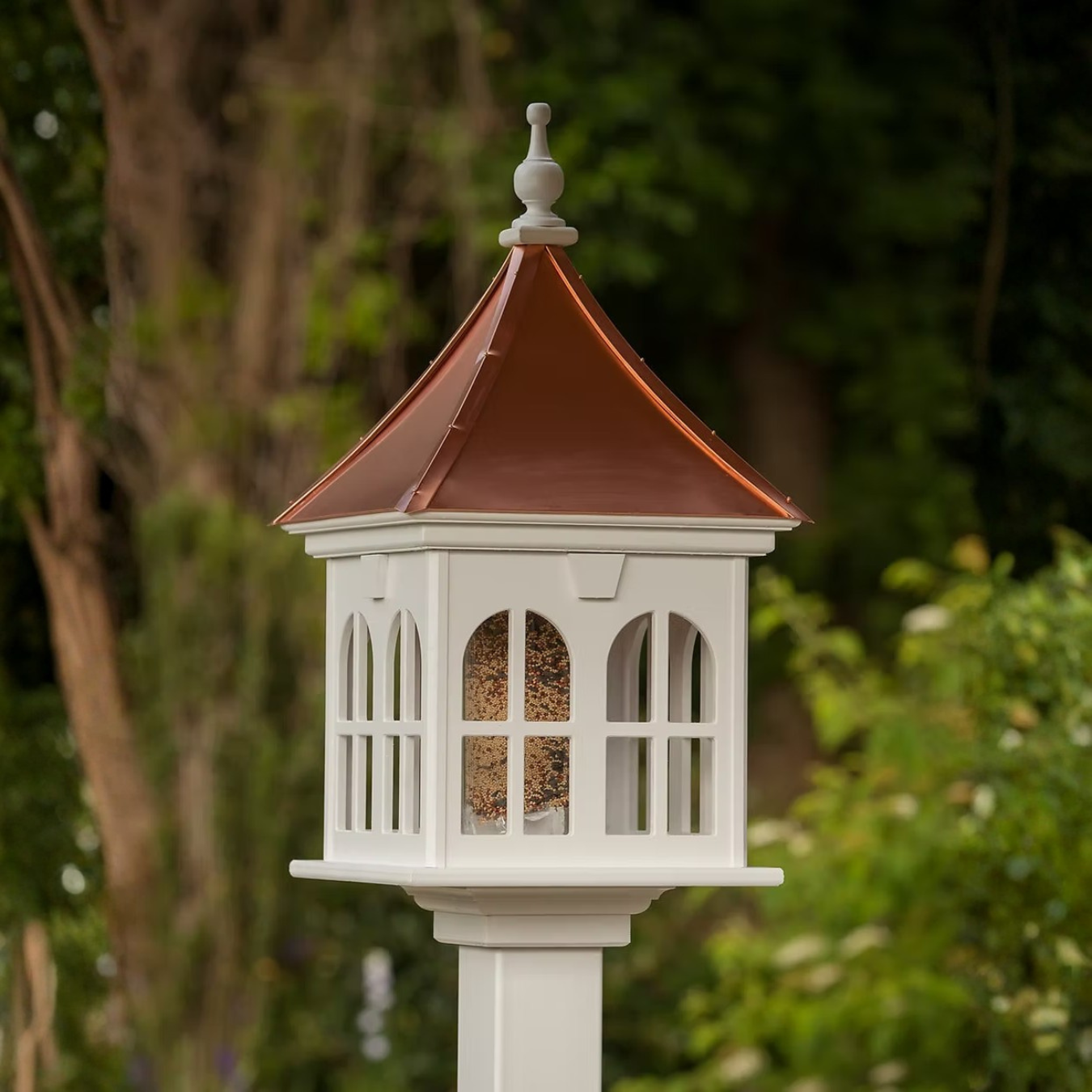 Decorative bird feeder with window panes and a copper roof against a green background