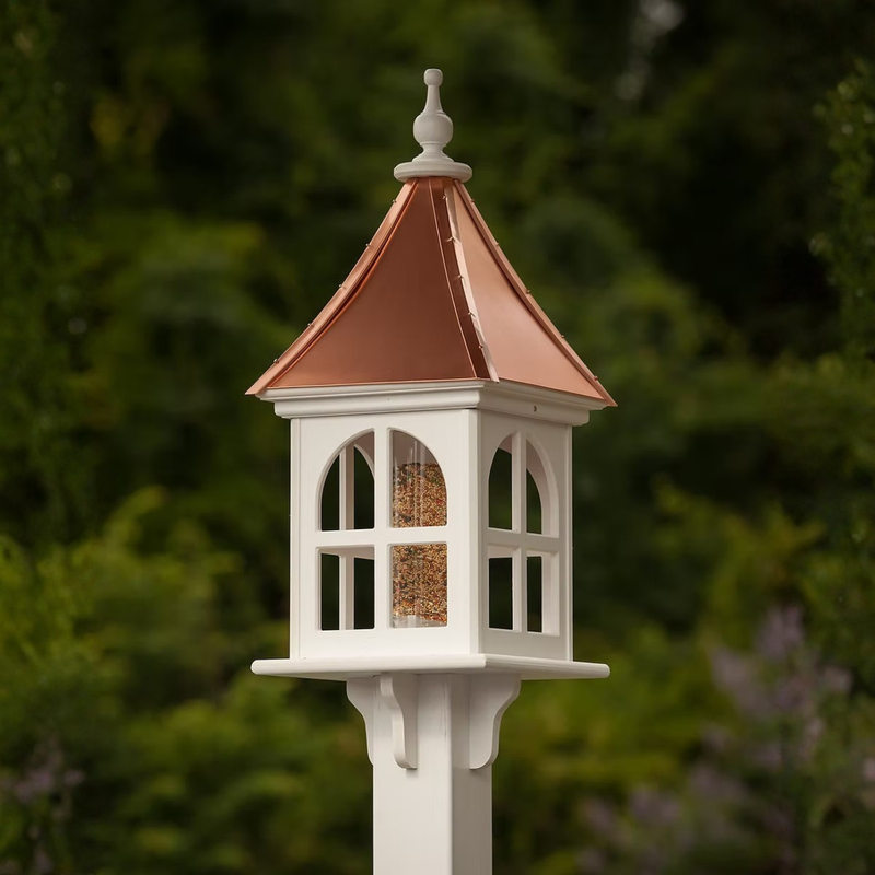 Decorative bird feeder with windows and a copper roof against a blurred green background