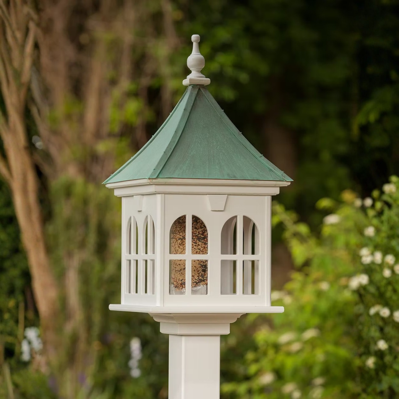 Decorative bird feeder with windows and a patina copper roof against a natural background