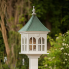Decorative bird feeder with windows and a patina copper roof against a natural background