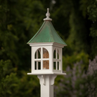 White bird feeder with windows and a  patina copper roof against a blurred natural background