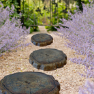  Set of log-style stepping stones arranged along a garden pathway, creating a rustic, natural look with a lush green background.