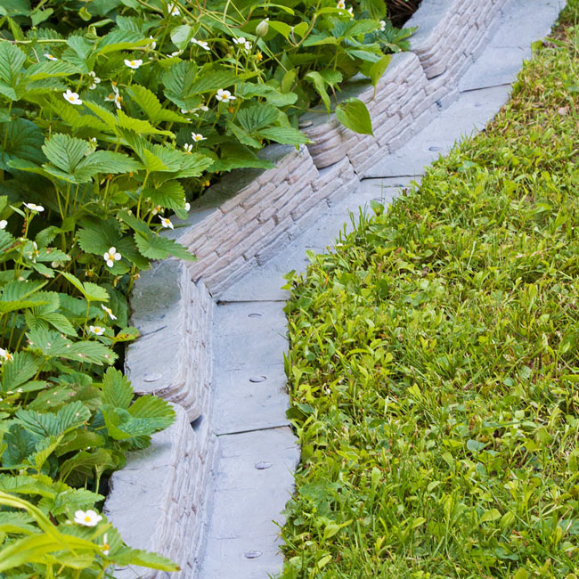 Stacked Stone Garden Border installed in a corner, showing the interlocking design and creating a natural stone appearance along the edge.