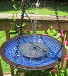 A solar-powered bird bath with a blue glazed ceramic edge and a black center, hanging from a chain, with water flowing up from the bottom creating a fountain effect.