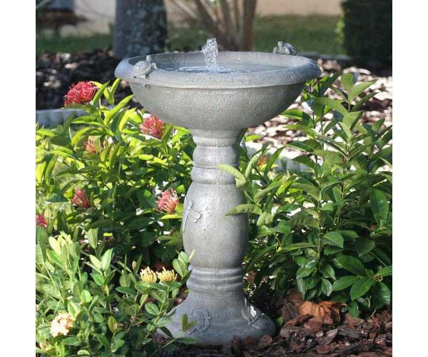 Country Gardens Solar Fountain Bird Bath in a garden with green and red flowers